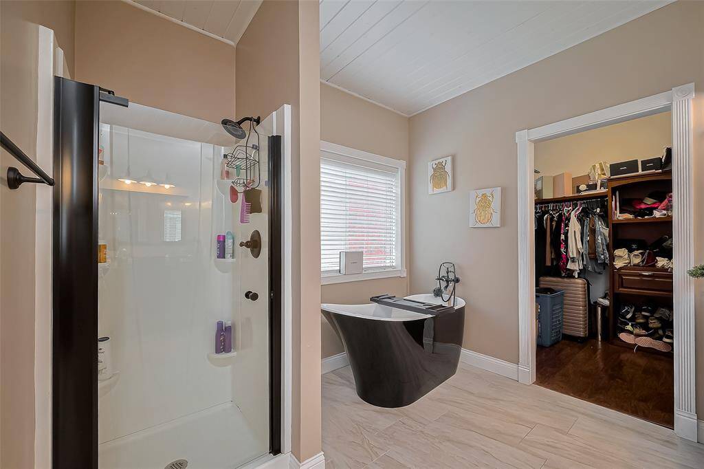 Primary modern bathroom with a sleek black freestanding bathtub, a glass-enclosed shower, and an adjacent walk-in closet. The neutral tones and natural light create a relaxing atmosphere.