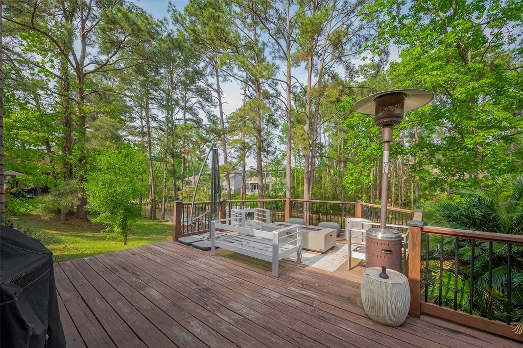 The spacious wooden deck with modern outdoor seating and a patio heater, surrounded by lush greenery and tall trees, offering a serene and private outdoor living space.