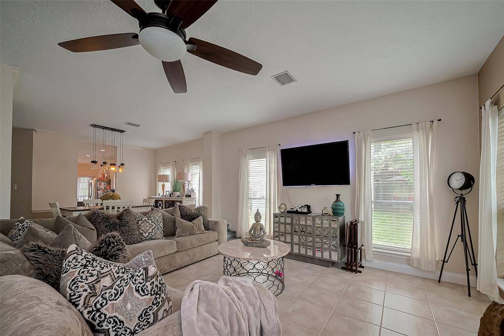 This spacious living room. Large windows allow plenty of natural light, and a ceiling fan adds comfort. The room is elegantly connected to a dining area, creating an open-concept feel, perfect for entertaining.