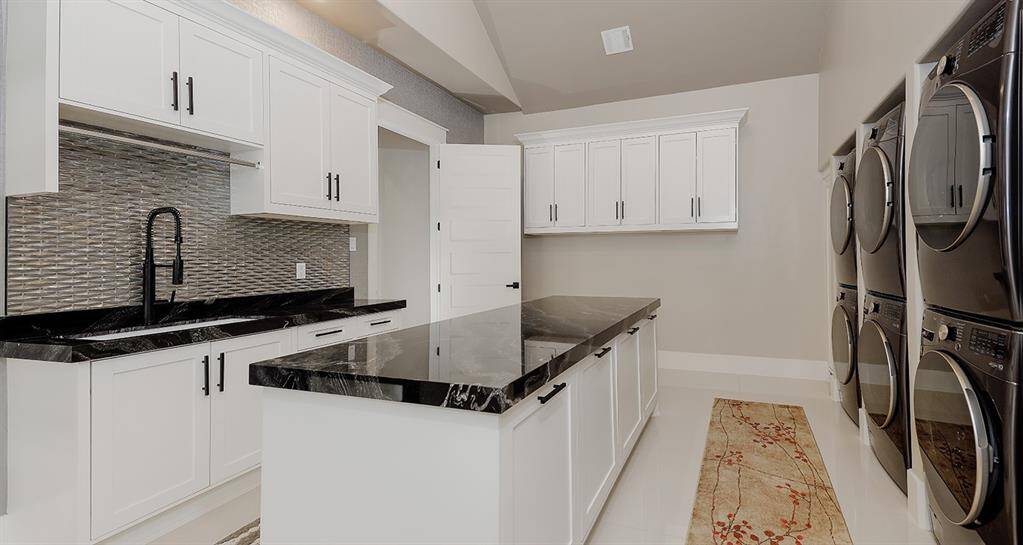 The main laundry room for the home features a folding island with quartzite counters, 3 stacked washers and dryers, and a sink.  There's more than enough cabinet storage and large formal porcelain tile floors.