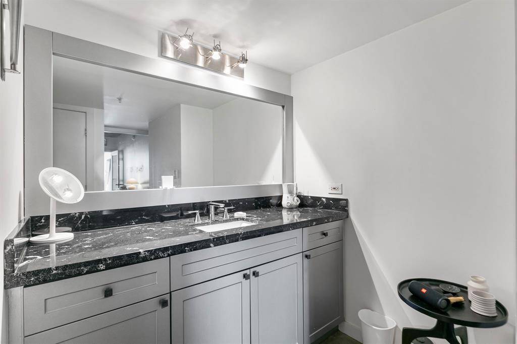Stylist primary vanity features stone counters and custom cabinetry accented with a modern mirror and pendent lighting.