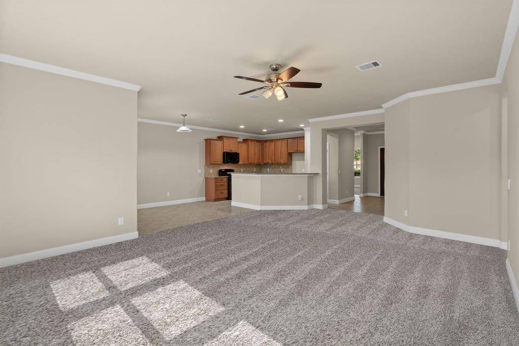 Plush new neutral carpet (coming 5/2!) sets the stage for comfort, while crown molding adds a touch of elegance throughout. Enjoy the breeze from the ceiling fan and a peek into the kitchen—complete with a high bar and warm-toned cabinets that invite you to stay awhile.