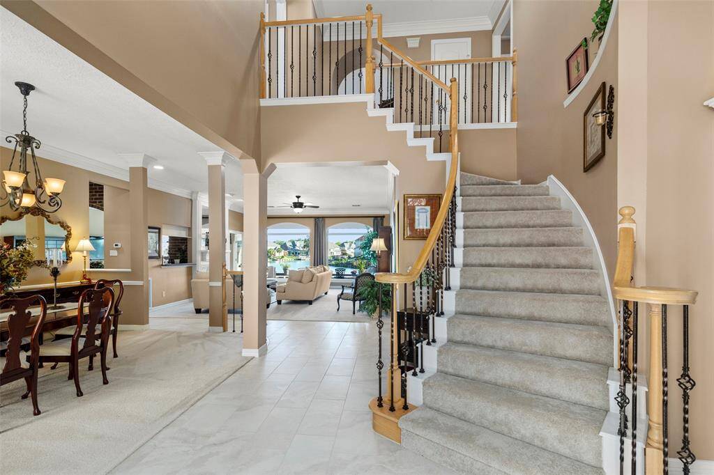 Inviting Entryway Features a Spacious, Light-Filled Dining Area with a Stylish Table and an Elegant Chandelier. Tiled Foyer Leads to a Spiral Staircase, Creating a Welcoming Atmosphere.