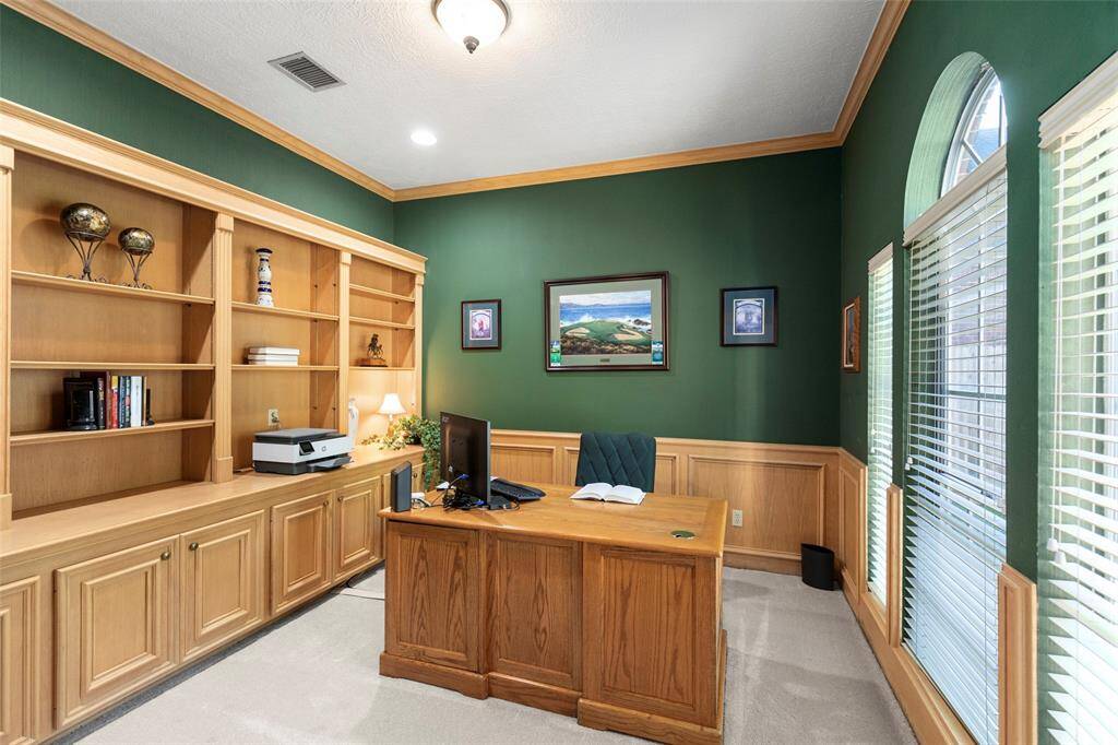 Showcases a Well-lit Home Office with Built-in Wooden Shelves, and a Large Window.