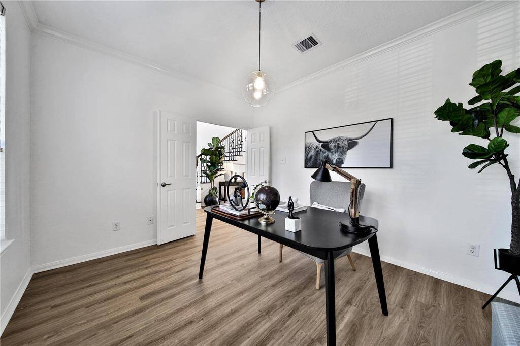 This home office features a minimalist design with a modern black desk, stylish lighting, and wood flooring. It has natural light from a large window.
