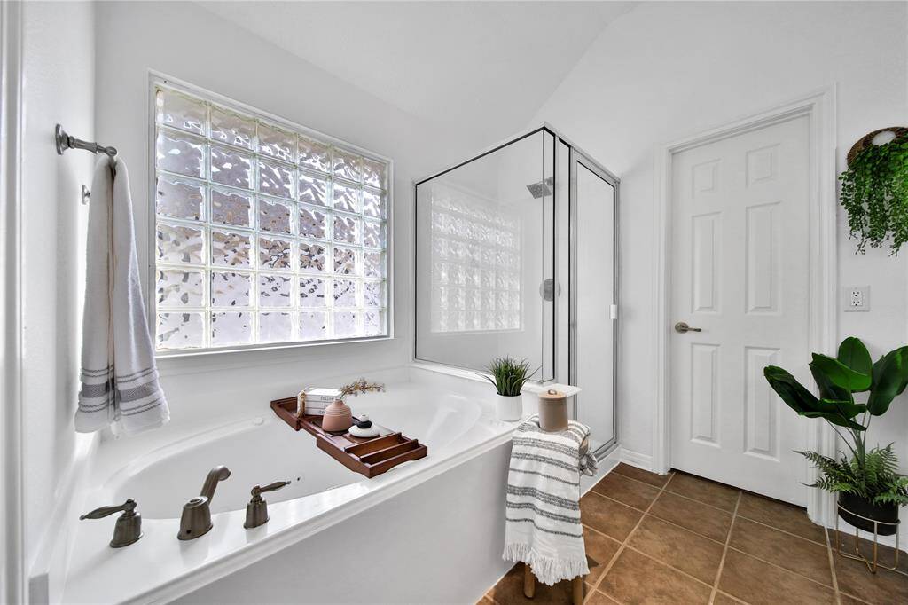This bathroom features a spacious tub with a sleek glass block window, a separate glass-enclosed shower, and tasteful decor. The neutral tones and natural light create a relaxing ambiance.