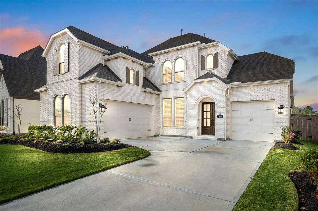 This elegant two-story home features a white brick exterior, two spacious garages, and a well-manicured lawn. The arched windows and front entrance add a touch of sophistication, while the ample driveway provides plenty of parking space.