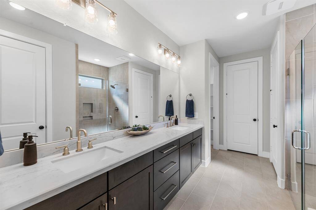 Walk-in glass enclosed shower with a bench seat, neutral tiled flooring and expansive vanity area offering tons of storage