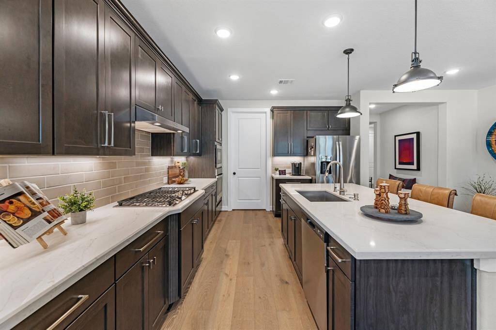 This kitchen has beautiful wood cabinets with crown molding and plenty of counter space. The quartz counters are neutral along with the wood flooring and stainless appliances. The corner pantry is a walk-in with shelving for great organization