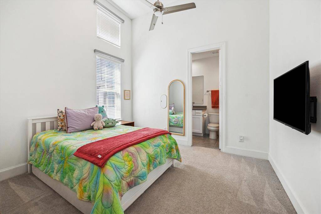 This third-floor guest suite offers a welcoming and comfortable space for both family and visitors. Highlights include a towering ceiling with a modern cooling fan, stacked windows that fill the room with natural light, plush carpeting, neutral paint, and ensuite access to a private bathroom and a spacious closet.