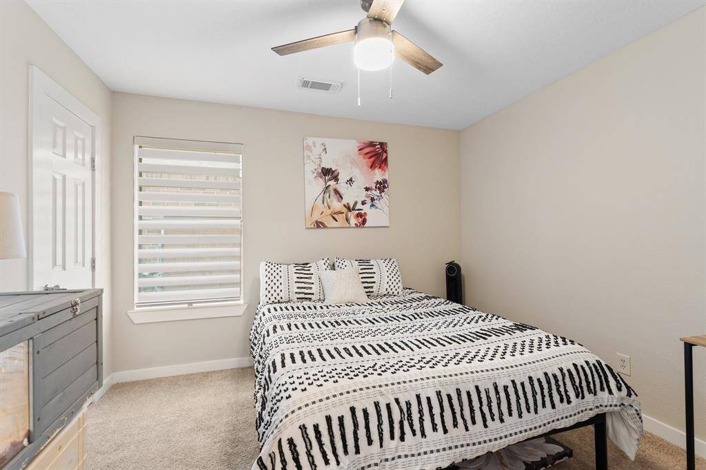 This inviting bedroom features plush carpet, a large window for natural light, and a sleek modern ceiling fan for added comfort.