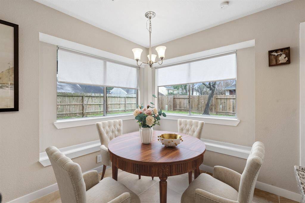 The charming breakfast nook boasts elegant tile flooring, a stylish chandelier, and two windows with privacy roller shades, creating the perfect cozy spot to start your day. *Virtually Staged*