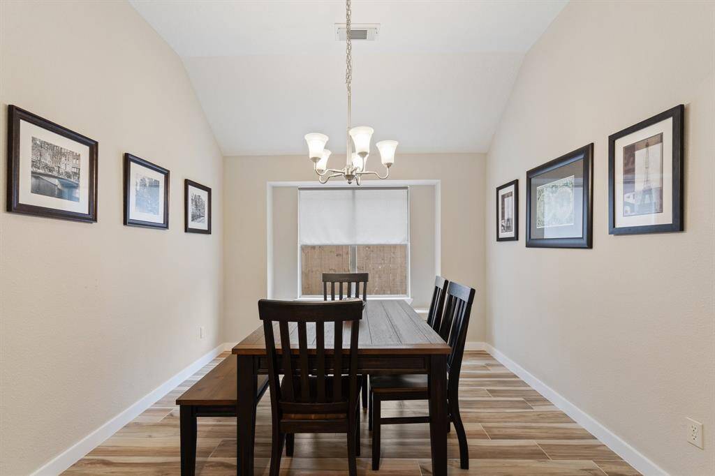 This inviting dining room boasts rich wood flooring, a large window with privacy shades that fill the space with natural light, and a stunning chandelier that adds a touch of elegance to every meal.