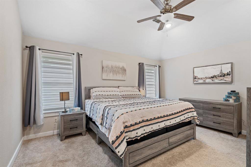 The primary bedroom boasts soaring high ceilings, two generously sized windows that bathe the room in natural light, and plush carpeting, creating a spacious and inviting retreat.