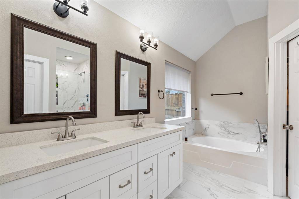 The primary bathroom offers a spa-like retreat with a luxurious large bathtub, a stylish double sink vanity with framed mirrors, and elegant tile flooring for a polished finish.