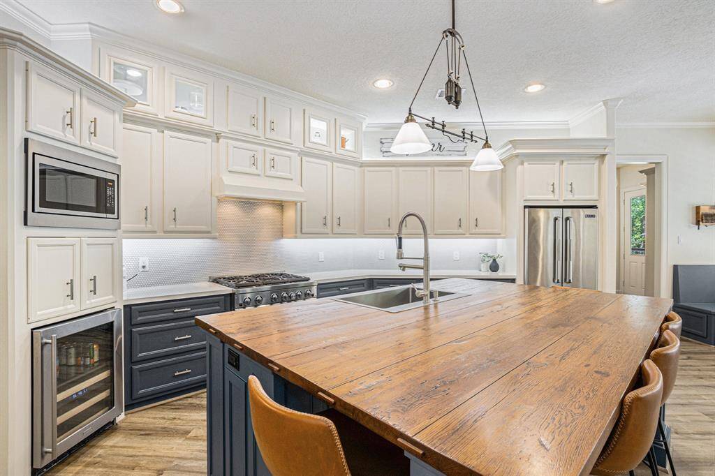 Chef-inspired kitchen presents a massive center island with breakfast bar seating, a beverage cooler, ample cabinet space, and a farm-style sink.