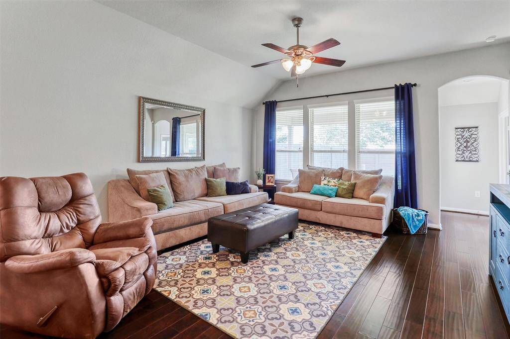 The spacious family room welcomes you with warm wood flooring, a vaulted ceiling with a cooling fan, and an abundance of natural light streaming through the wall of windows overlooking the backyard.