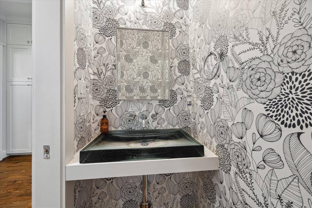 The stylish powder bath makes a bold statement with custom floral wallpaper and a sleek glass vessel sink — a perfect blend of personality and modern design.