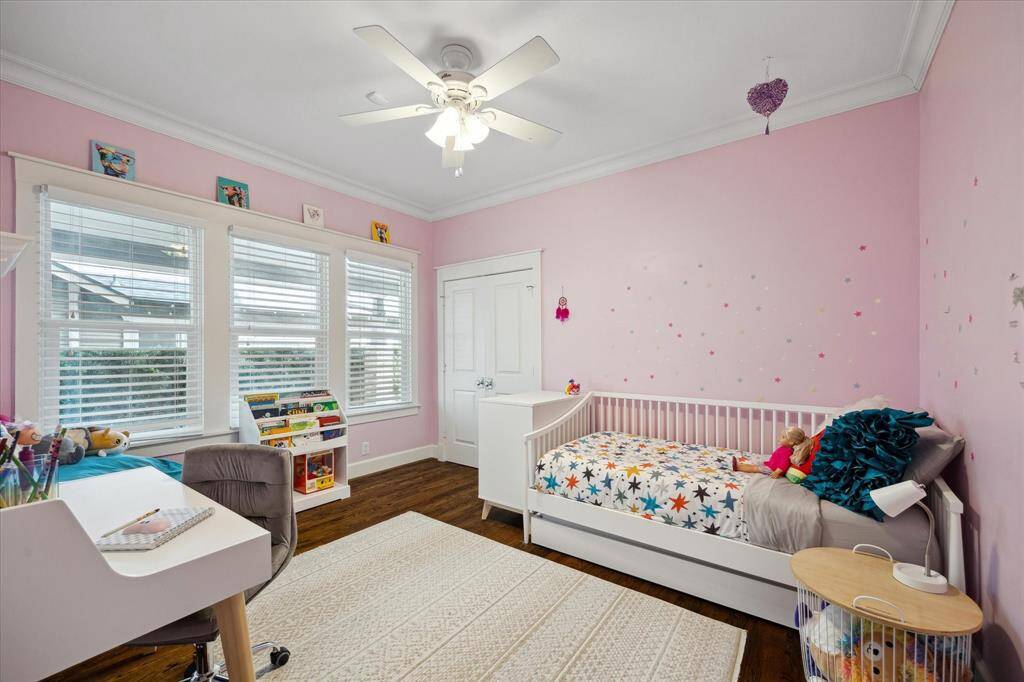 A cheerful and spacious secondary bedroom with playful pink walls, large windows for natural light, and plenty of room to sleep, play, and study.