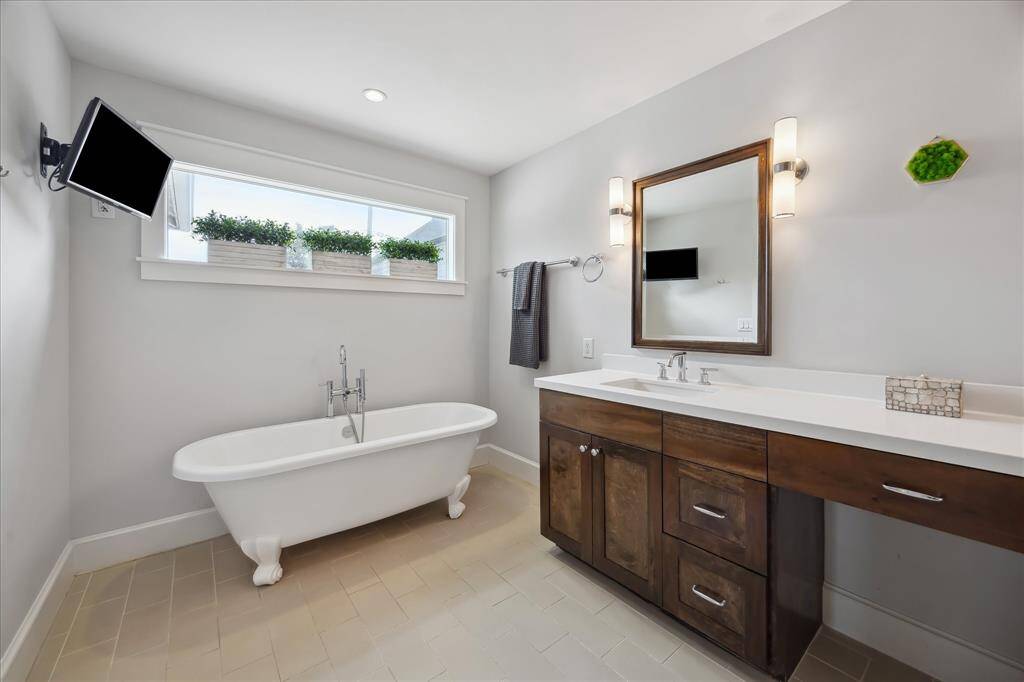 The spa-like primary bathroom offers a relaxing retreat with a classic clawfoot soaking tub, sleek modern lighting, and a large vanity with ample counter space and storage.