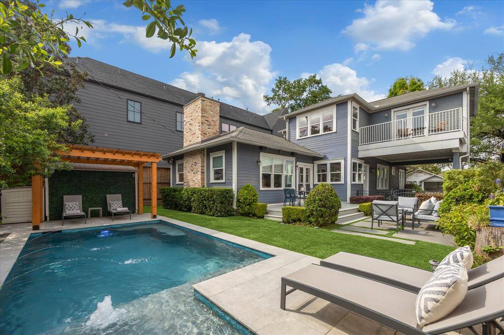 From the poolside, take in the charm of the home’s rear elevation, complete with multiple lounging areas, a raised deck, and a covered carport above which sits the second-floor balcony.