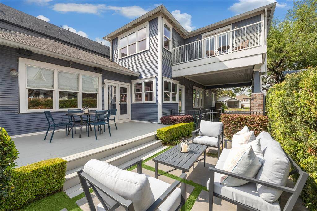 Another angle of the outdoor living area highlights the comfortable lounge setup, fresh landscaping, and sightlines to both the pool and the second-floor balcony above, tying the whole backyard oasis together.