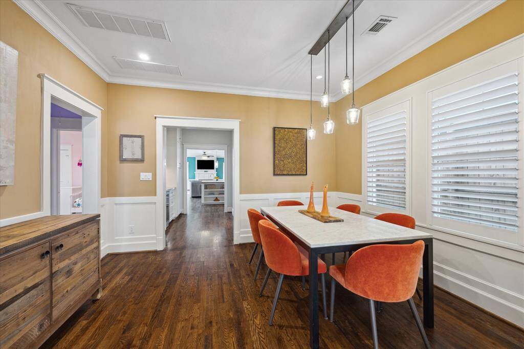 The formal dining room features rich hardwood floors, custom wainscoting, and stylish pendant lighting — all beautifully lit by natural light pouring through plantation shutters.