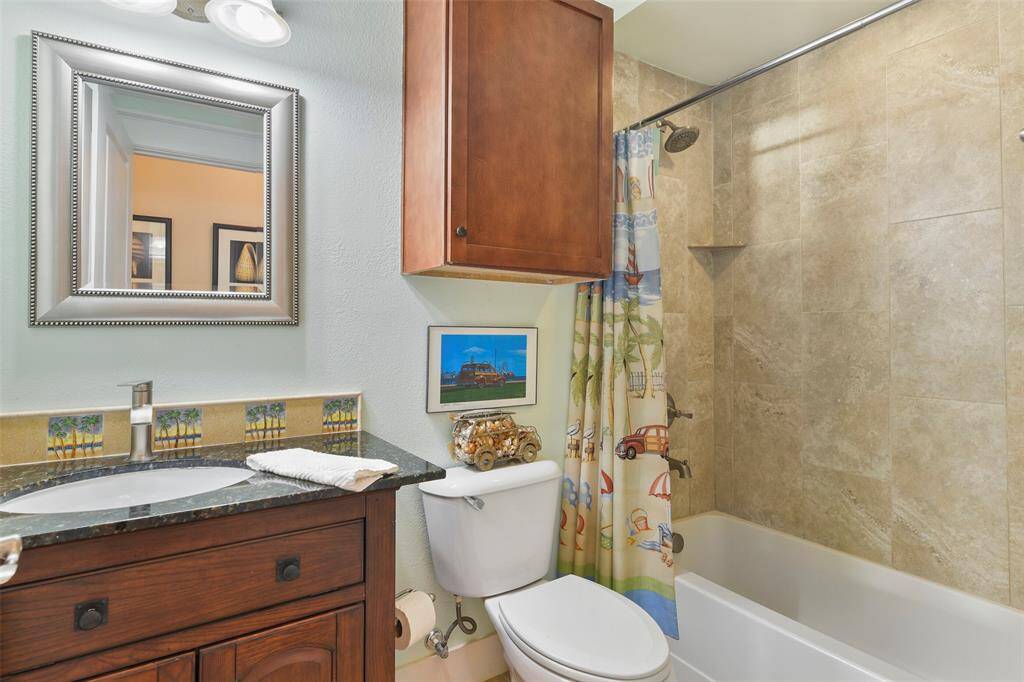 Shared hall bath with a custom vanity, granite, and beachy tiled backsplash. This bathroom also features a tub/shower combination with tile surround & nickel fixtures.