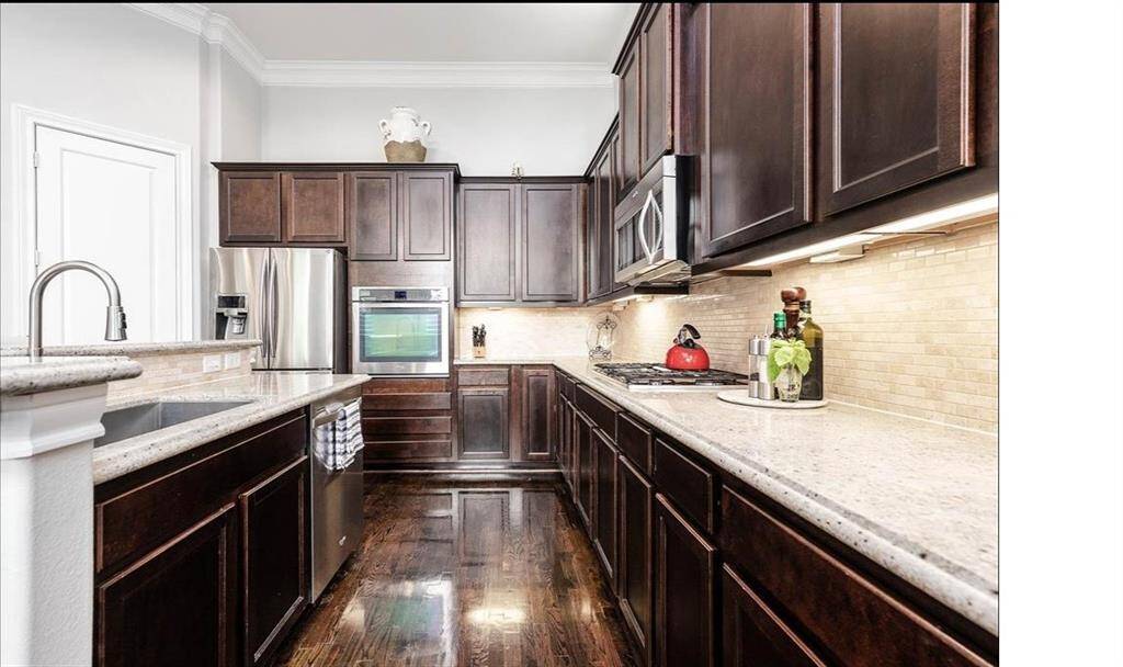 Beautifully designed kitchen with rich dark brown wood cabinetry, sleek stainless steel appliances, a gas cooktop, and a tall standing oven for easy access when baking – a chef’s dream space for both cooking and entertaining. Walk in pantry is to your left.