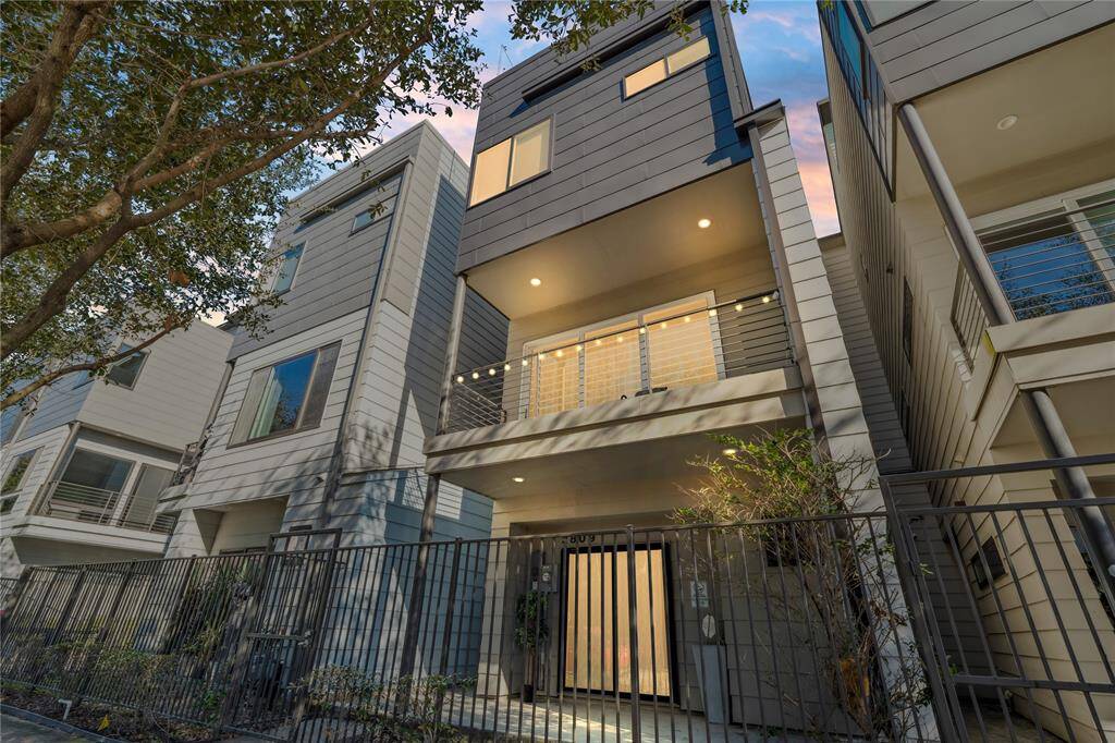 This contemporary three-story townhome with a rooftop terrace boasts a sleek modern facade with a mix of light gray siding and dark metal paneling, creating a stylish yet timeless appeal.