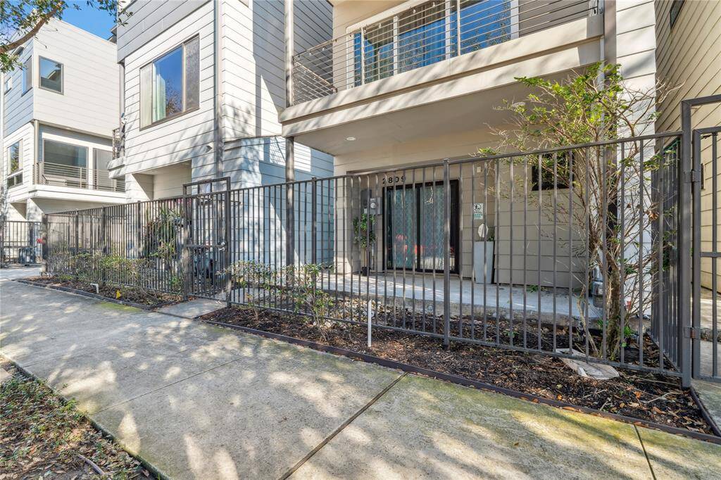 A private gated entrance leads to the front door, framed by a small landscaped area with lush greenery.