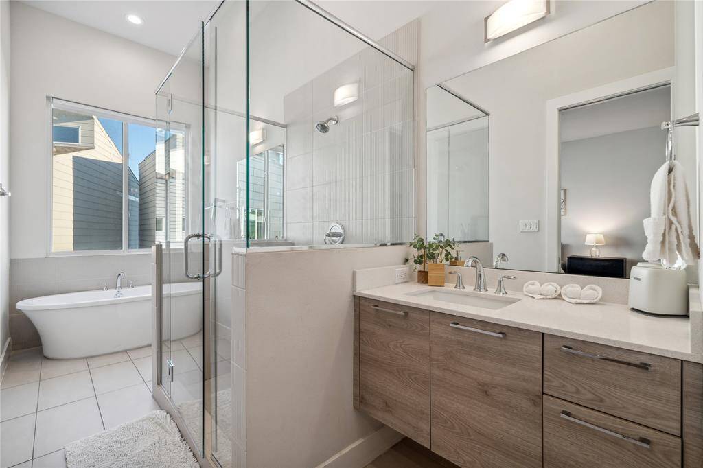 A spa-like ensuite bathroom includes dual vanities, a soaking tub, a walk-in shower with modern glass doors, and sleek tile finishes.