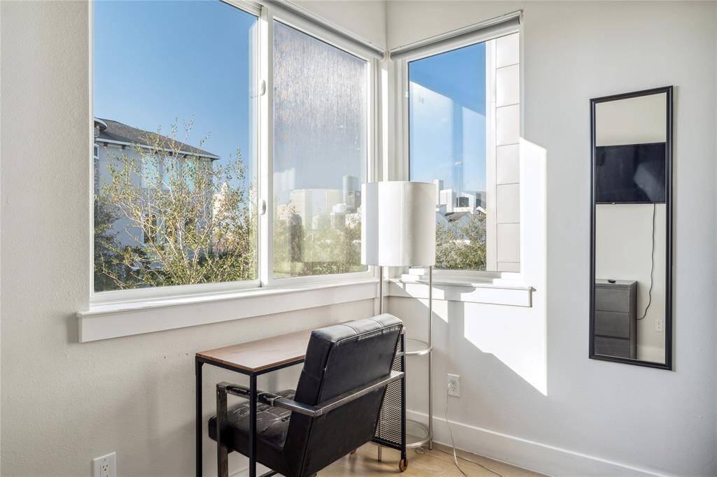 The secondary room features a cozy area, perfect for relaxation, reading, or additional functionality. Positioned near large windows, this space is bathed in natural light, creating a bright and airy ambiance.