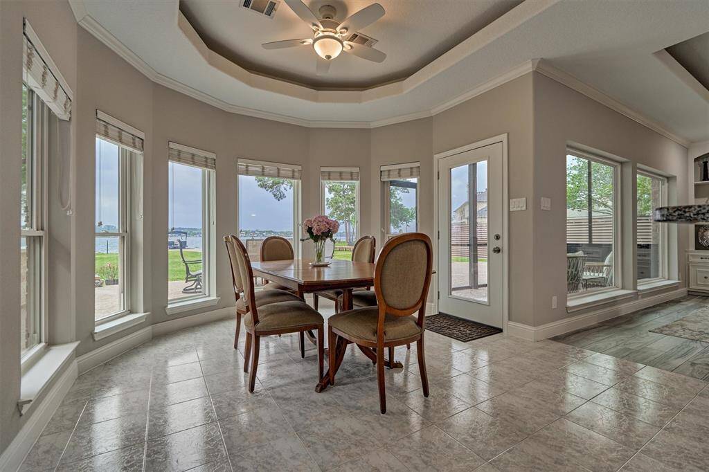 The breakfast nook features thoughtfully placed windows that capture the surrounding views from every angle. A glass door leads to the screened-in porch, extending the living space outdoors. The tray ceiling mirrors the design in the living room, creating a cohesive and elegant aesthetic throughout.