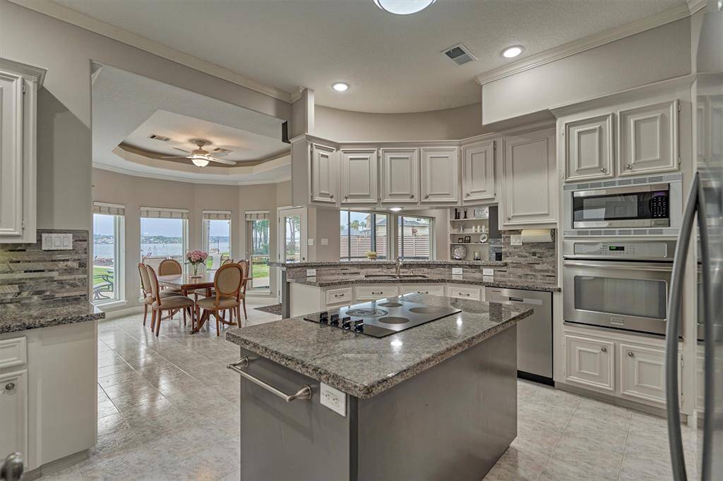 Another kitchen view shows the central island with built-in cooktop, perfect for meal prep and casual dining. The dark gray island complements the tile backsplash and granite countertops, creating a cohesive and stylish designer look.