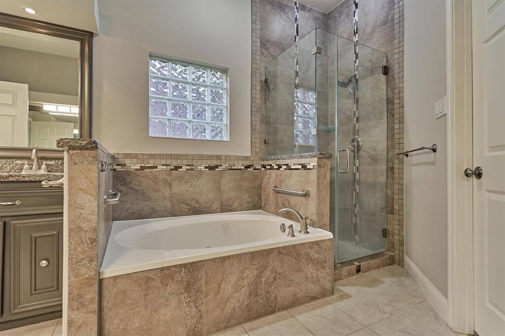 A separate soaking tub and a seamless glass shower, both accented by designer tile, create a luxurious and spa-like atmosphere.