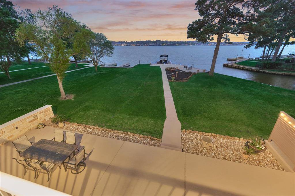 From the second-floor balcony, enjoy sweeping 180-degree views of the lake and beautifully manicured yard. This vantage point also highlights the paved walkway leading to the boat slip and the spacious decking area below.