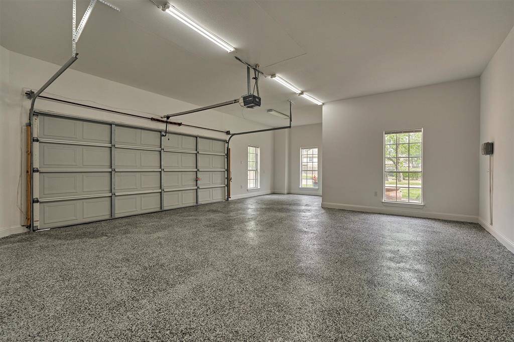 The two-car garage features a sleek epoxy floor finish, windows with views of the front yard, and a dedicated space perfect for a golf cart or workshop.
