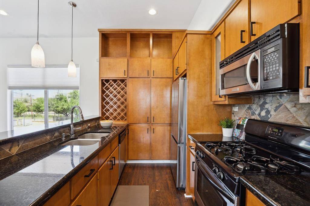 This well-appointed kitchen blends style and functionality with granite countertops, slate tile backsplash, and sleek stainless steel appliances. Ample cabinetry with modern pulls offers plenty of storage, while built-in wine storage and elegant pendant lighting add a touch of sophistication.