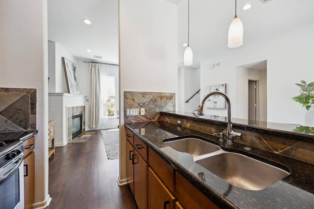 A spacious extended bar creates a natural divide between the kitchen and dining area, complete with ample storage below, deep basin sinks with a pull-down fixture, bar seating for casual dining or conversation, and sleek pendant lights overhead.