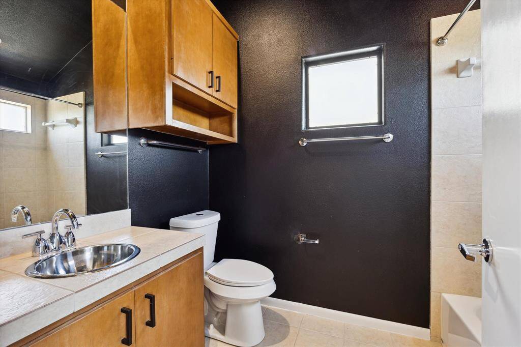 The guest ensuite bathroom features a single-sink vanity, convenient over-the-john storage, and a fully tiled tub/shower enclosure—combining comfort and functionality for visiting guests.
