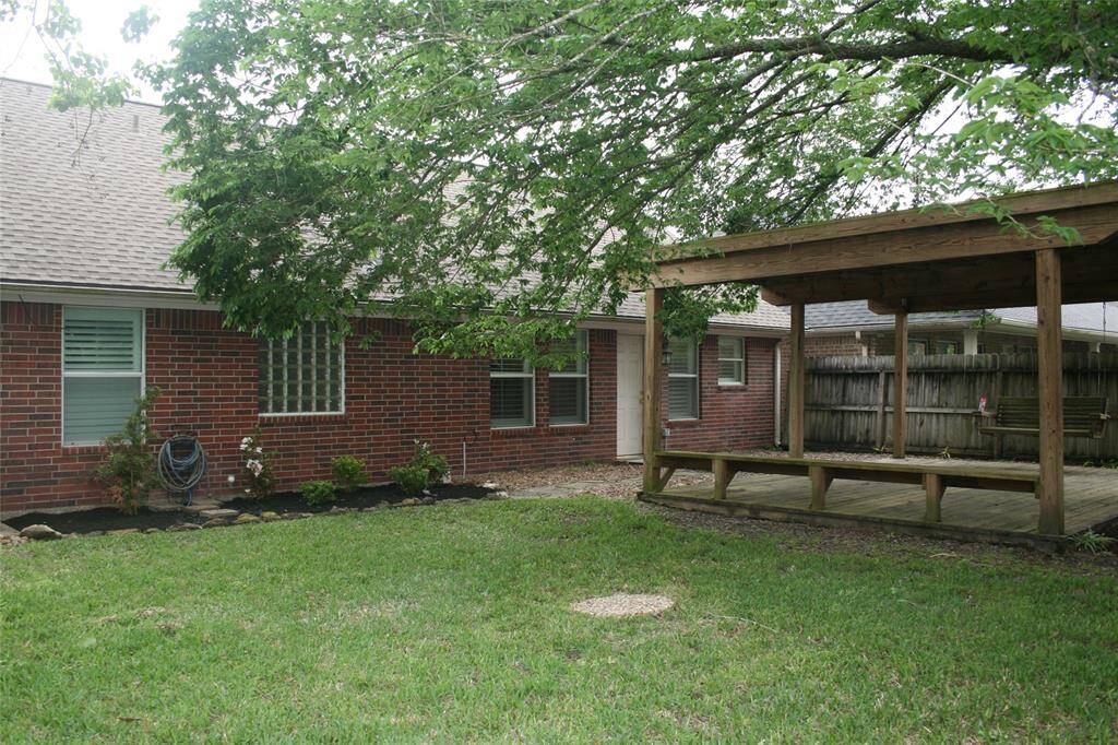 Another view of the back yard with large pergola, oak tree and sprinklers.