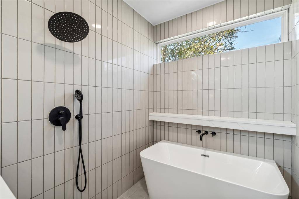 Modern shower and bath combination featuring a sleek freestanding soaking tub, rainfall showerhead, and floor-to-ceiling contemporary tile design with a clerestory window for natural light and privacy.