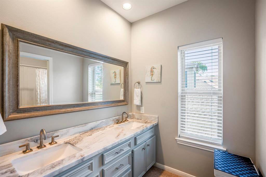 One of the secondary bathroom upstairs, dual sinks, gorgeous framed mirror, and overhead lighting, large window with blinds.
