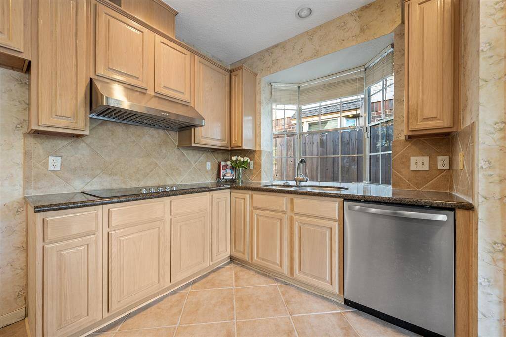 Kitchen features light wood cabinetry, granite countertops, and stainless steel appliances, including a cooktop and dishwasher. A large window above the sink provides ample natural light.