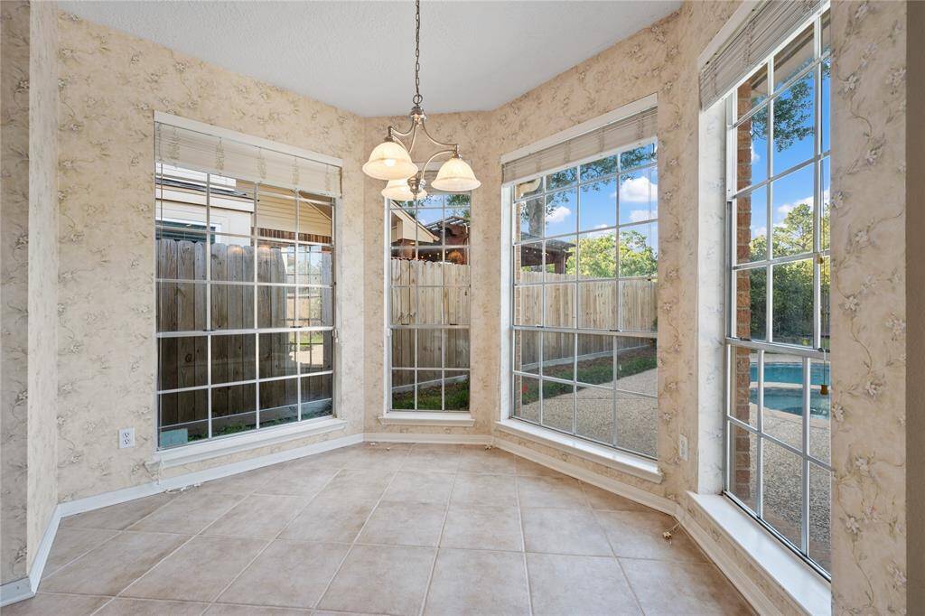 Bright breakfast nook with large windows, tiled floor, and a view of the backyard and pool area.