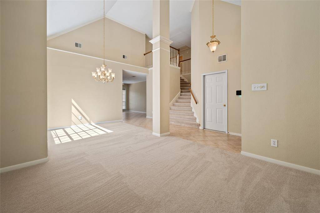 This spacious home features high ceilings and a well-lit open floor plan with neutral tones. The carpeted area flows into a tiled section leading to a staircase, adding a touch of sophistication.