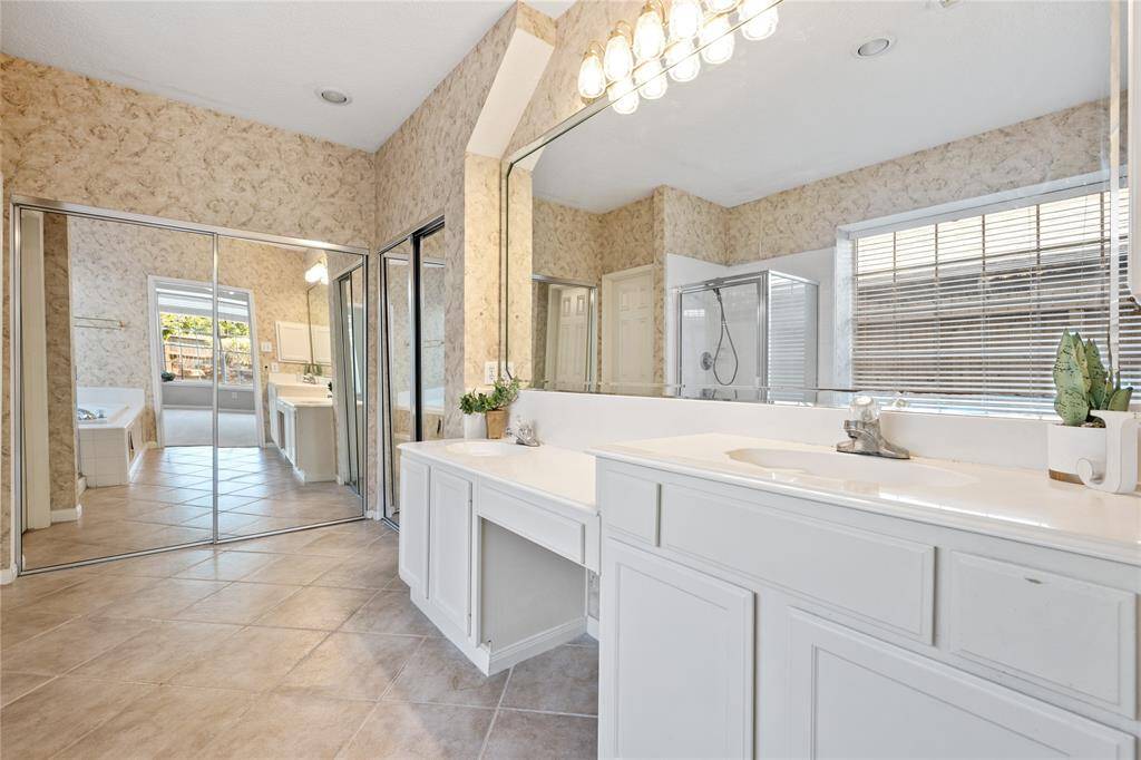 Spacious primary en-suite bathroom features a large dual-sink vanity and ample storage. It includes a glass-enclosed shower, a separate bathtub.