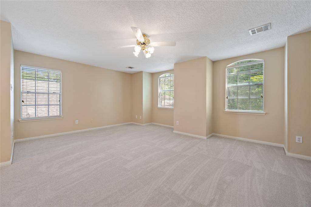 Huge carpeted game room with neutral walls, featuring three large windows for natural light.