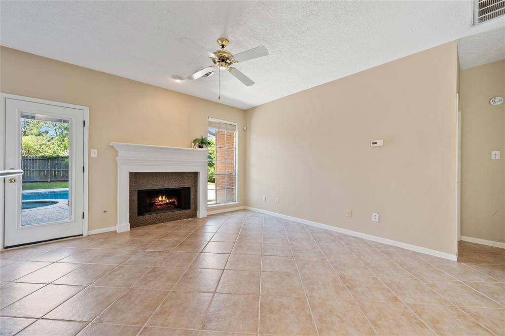 Bright living room with tiled floor, cozy fireplace, and ceiling fan. Features a door leading to a backyard with a pool.